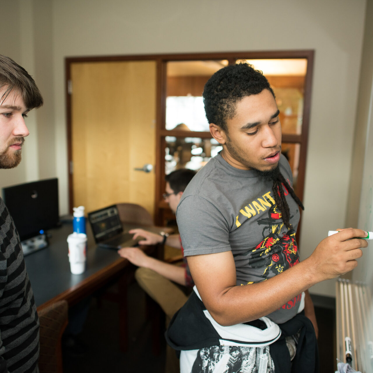 One student drawing a plan on a white board, while anoter student analyses it. 