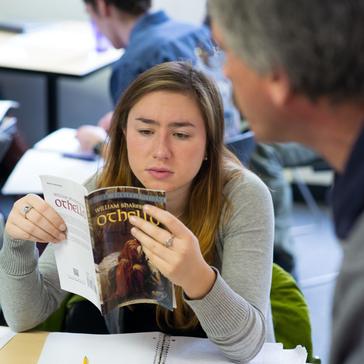 Student studying her copy of Othello while taking notes during class.