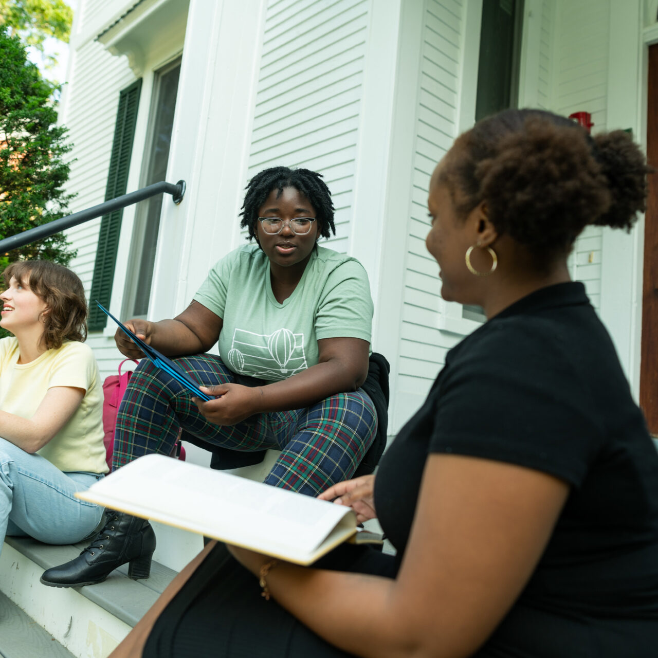 Three people discussing paperwork while on a dorm's porch